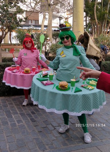 Zwei Personen in bunten, kuchenähnlichen Kostümen mit Snacks und Getränken.